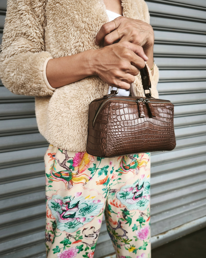 Person holding a brown handbag wearing a beige fleece jacket and floral pants.