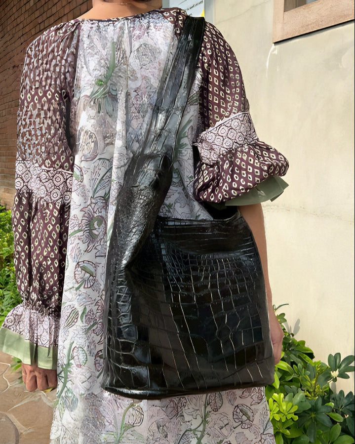 Person wearing a patterned outfit with a black bag, standing outdoors.