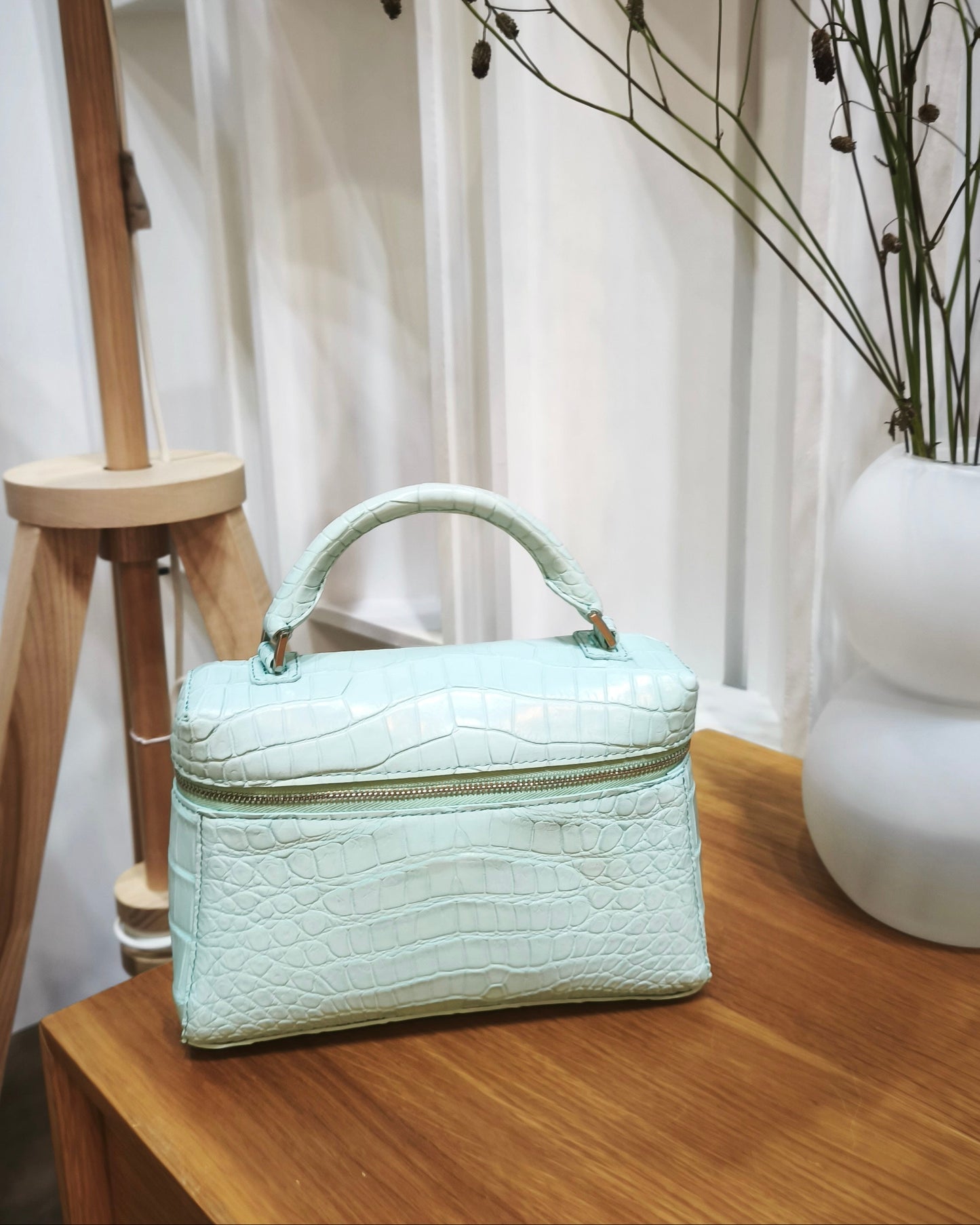 Light blue handbag on a wooden surface with a white vase and decorative branches in the background.