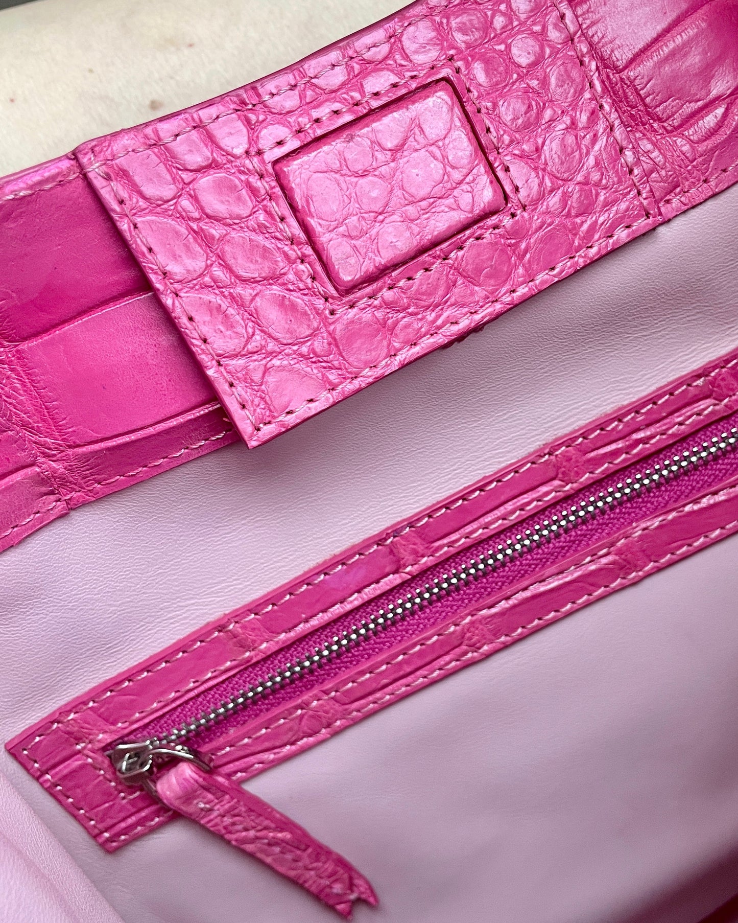 Close-up of a pink handbag with a zipper and crocodile texture.