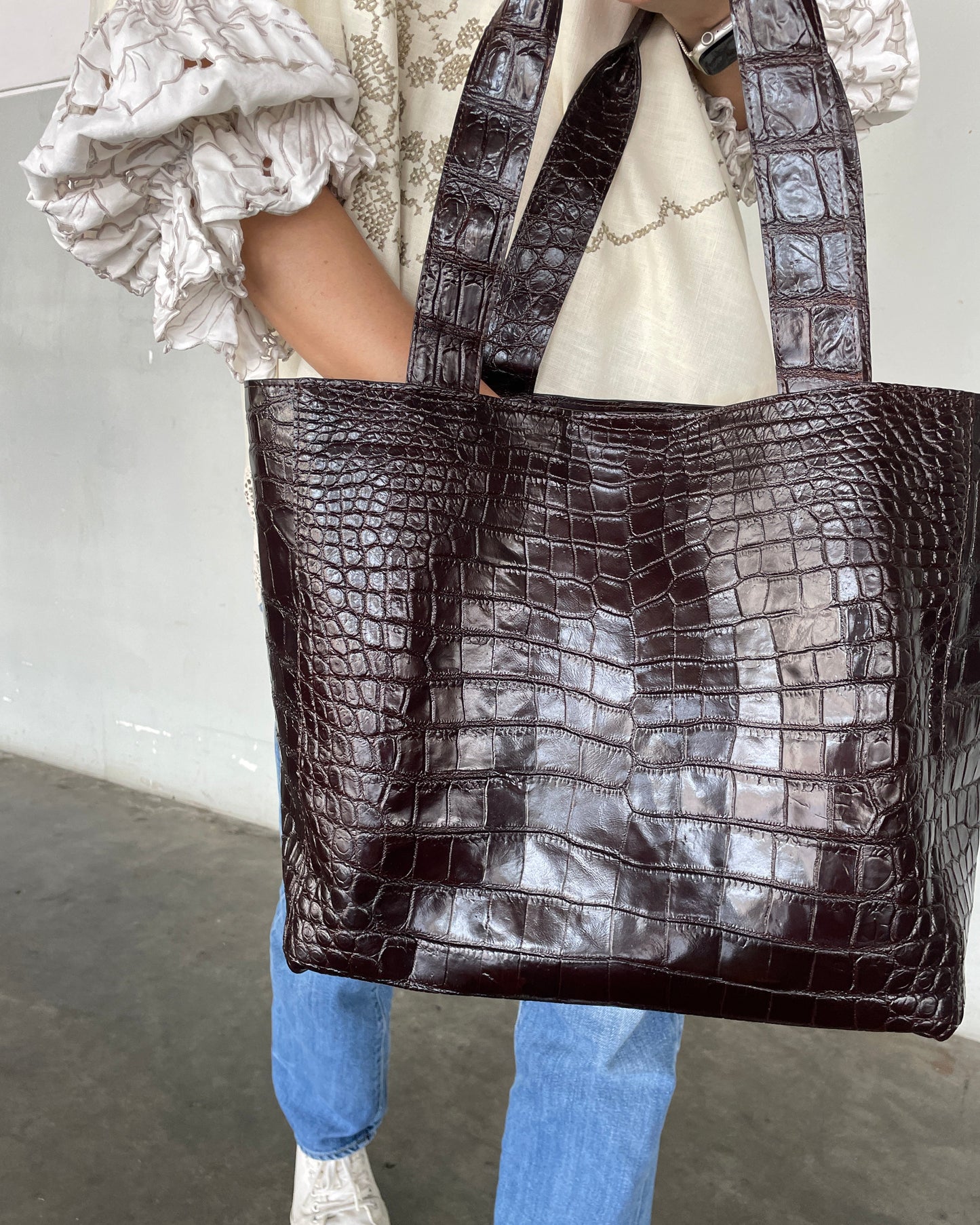 Person holding a large brown crocodile-patterned bag with a neutral background