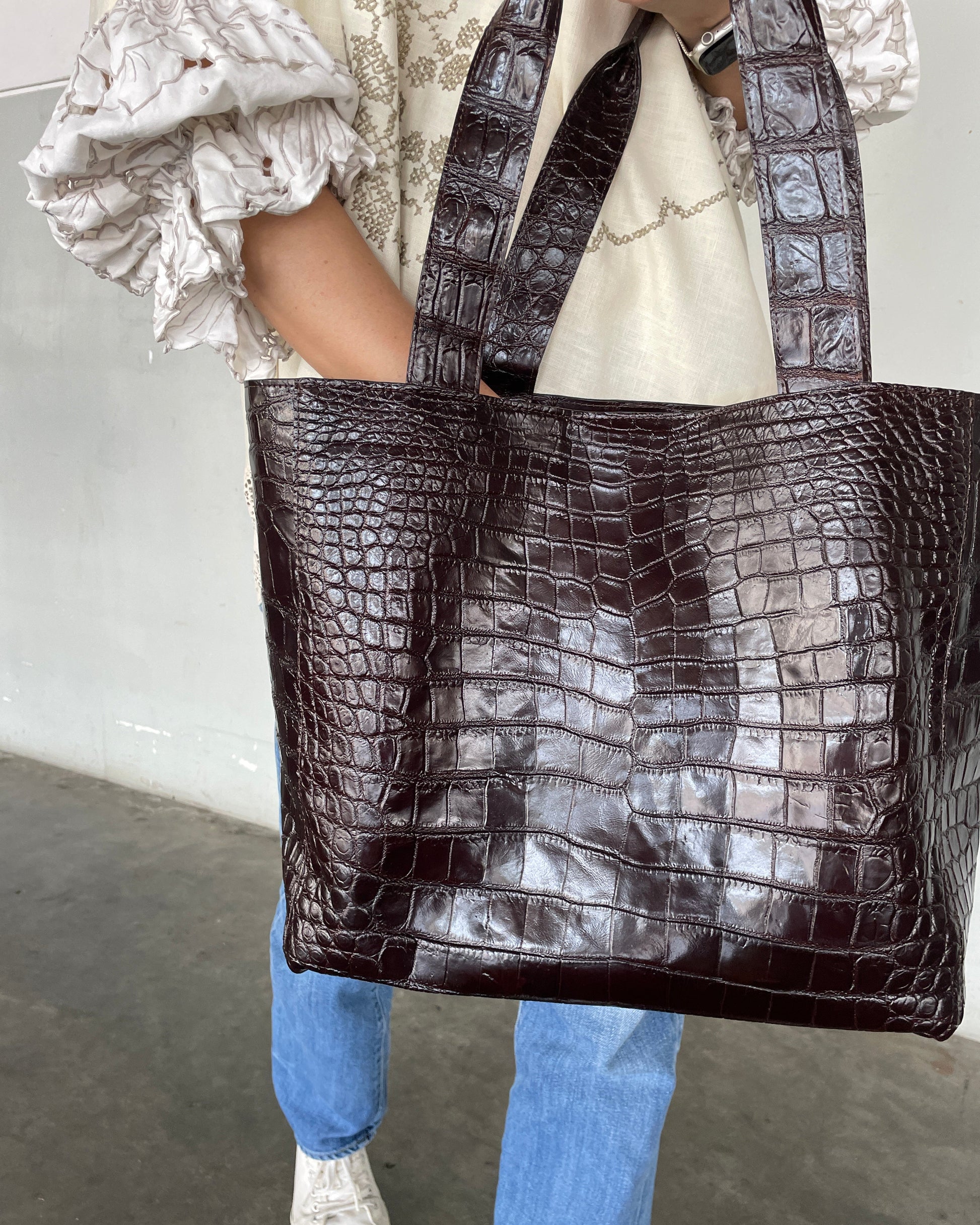 Person holding a large brown crocodile-patterned bag with a neutral background