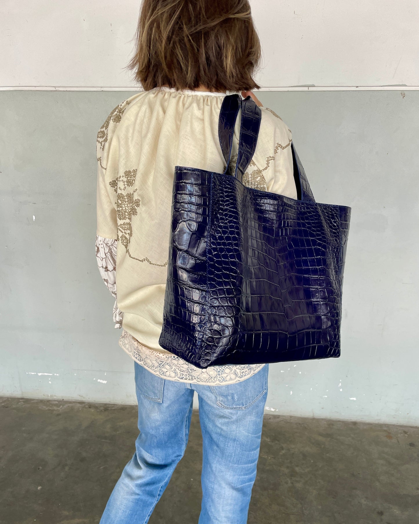 Person wearing a navy blue crocodile-patterned tote bag against a plain background