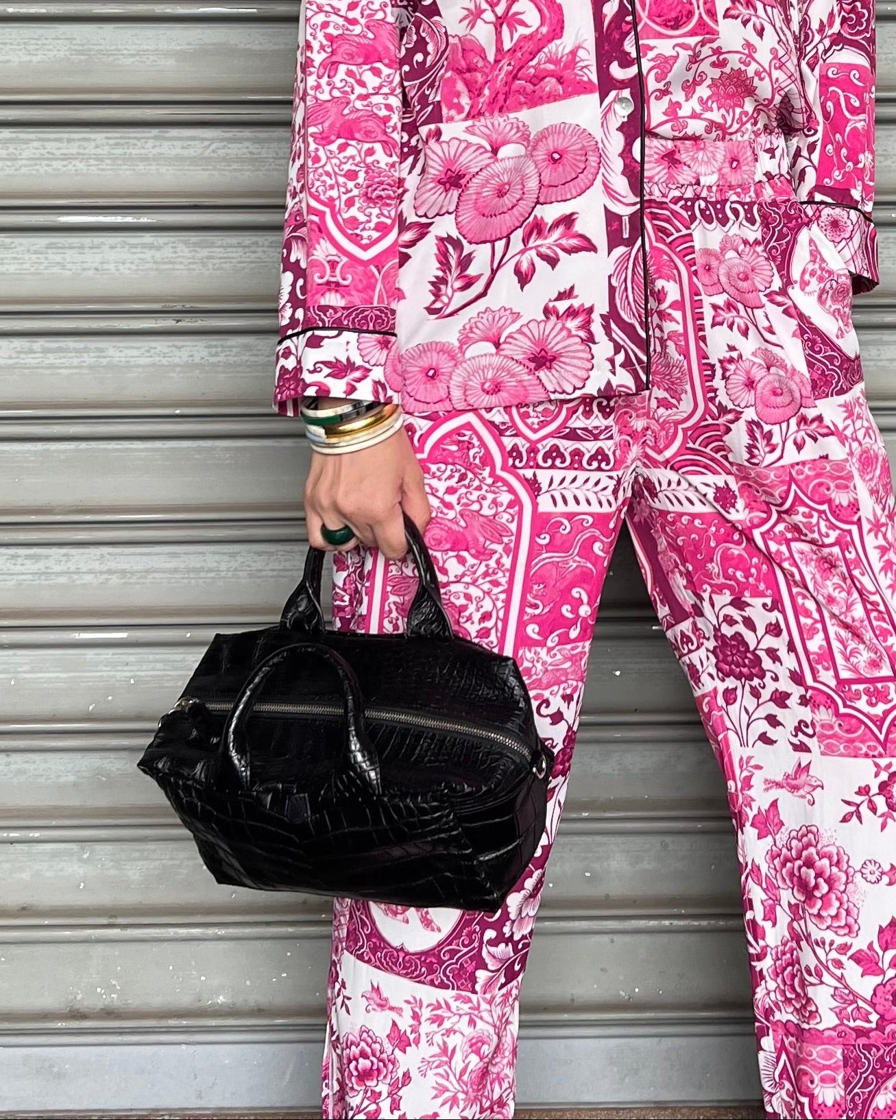 A person wearing a pink floral patterned suit and carrying a black crocodile leather top handle bag.
