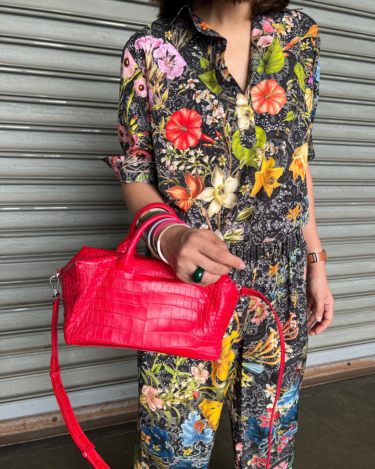 Person wearing a colorful floral dress holding a red handbag on a striped background
