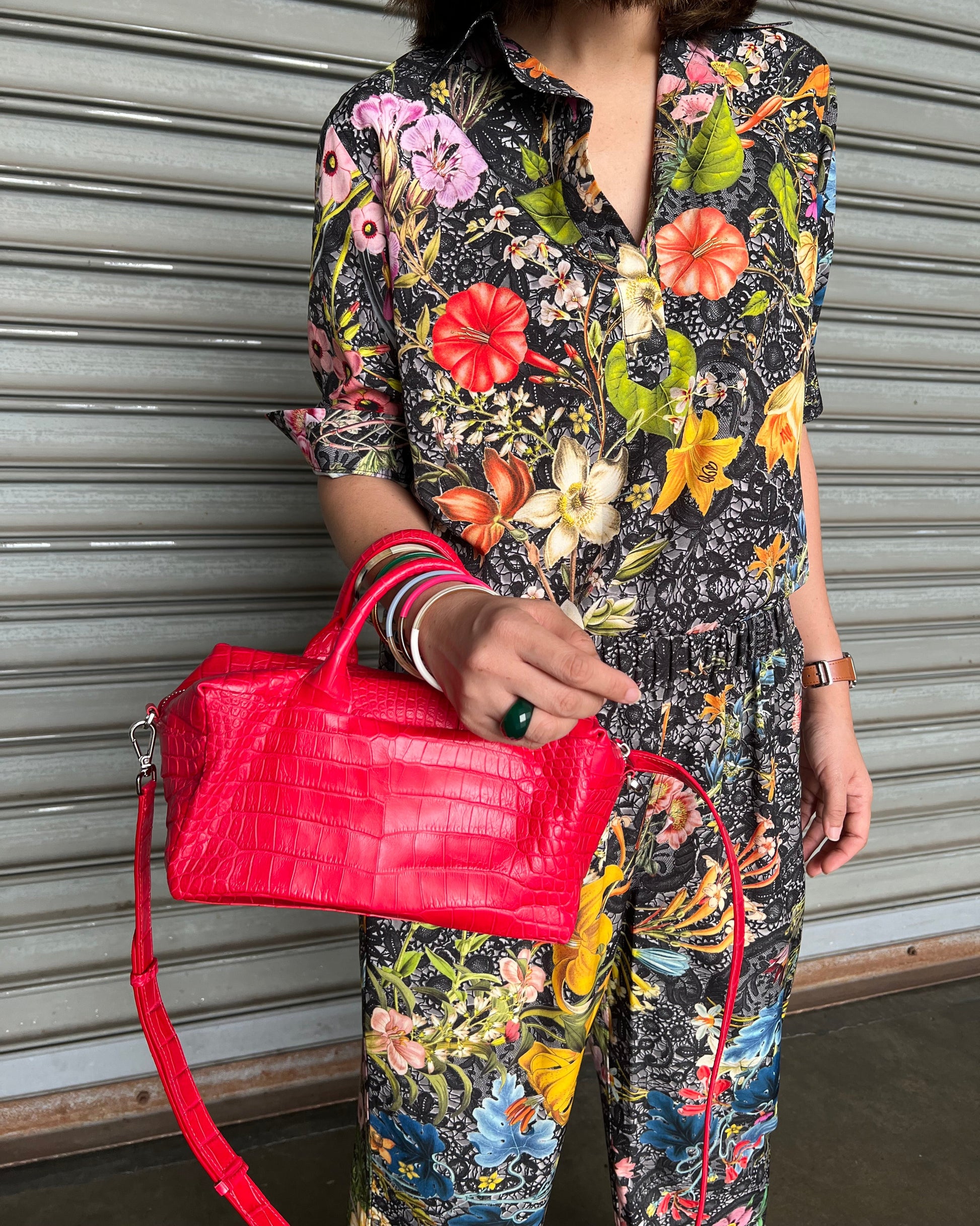 Person wearing a colorful floral dress holding a red handbag on a striped background