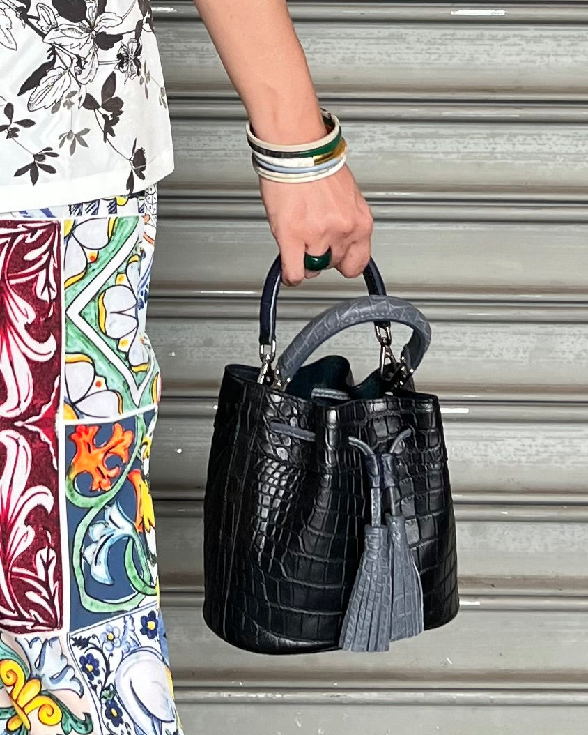 Person holding a black handbag with tassels against a metallic background