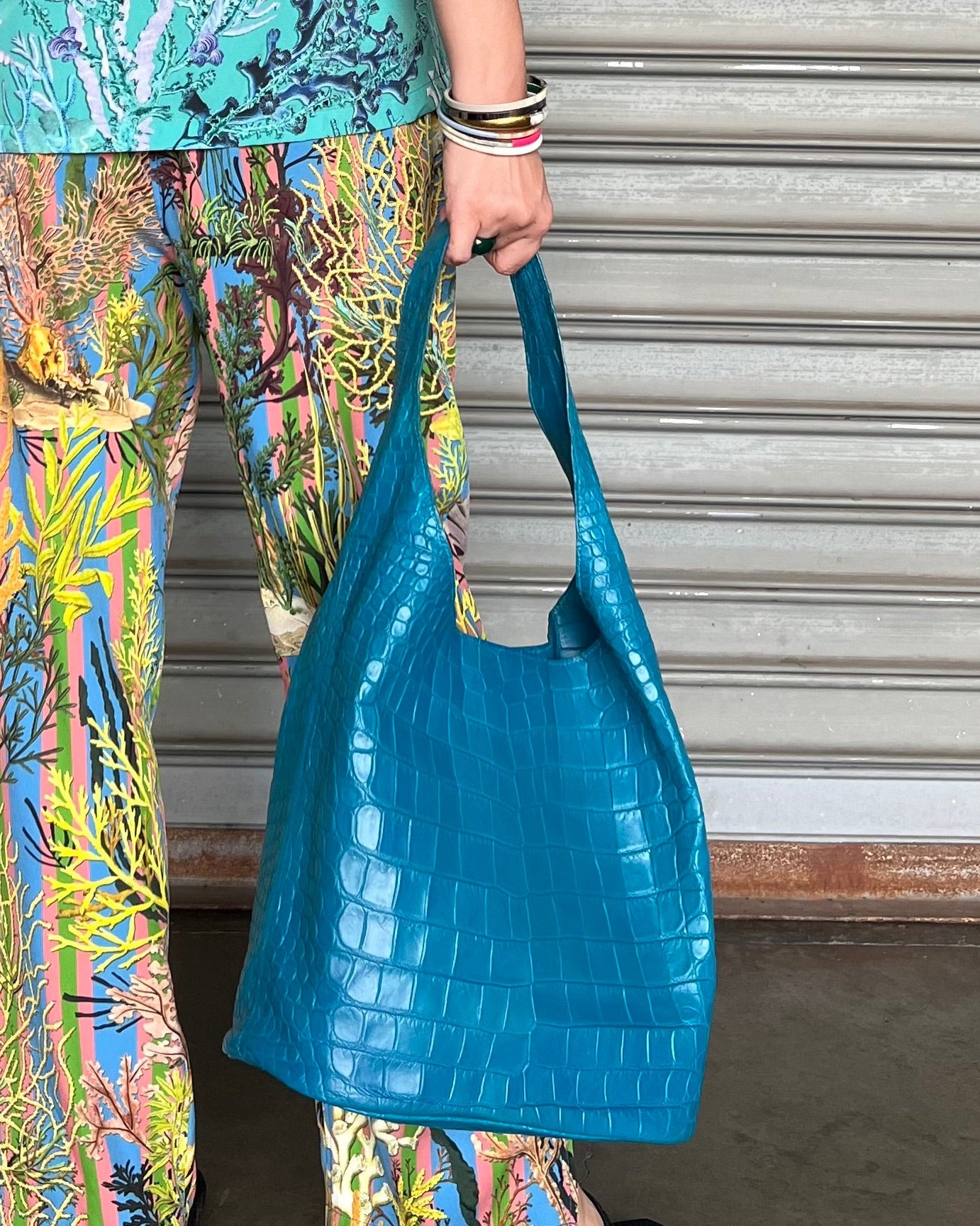 Person holding a blue handbag in front of a metallic shutter.