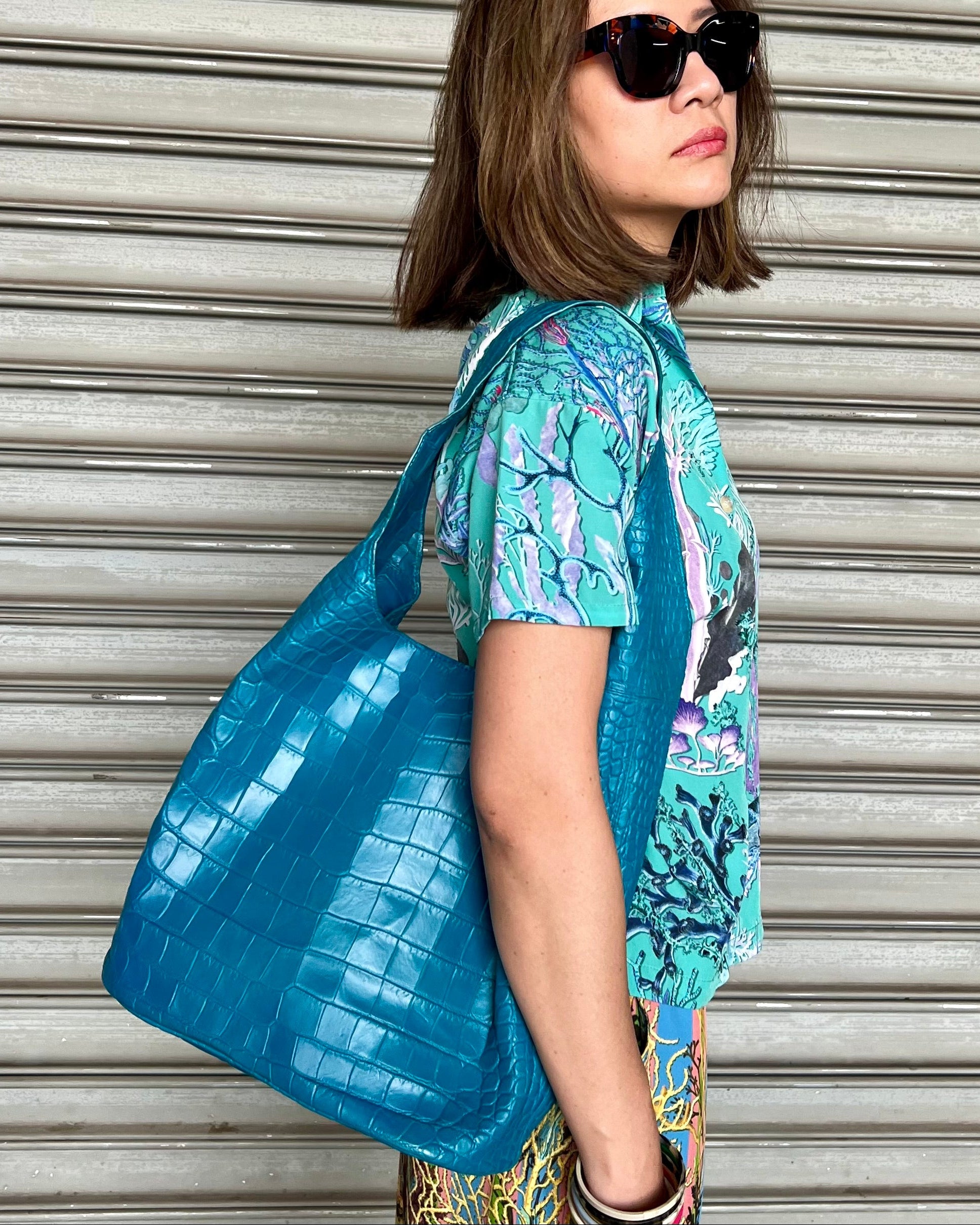 Woman holding a blue textured bag against a metallic shutter background