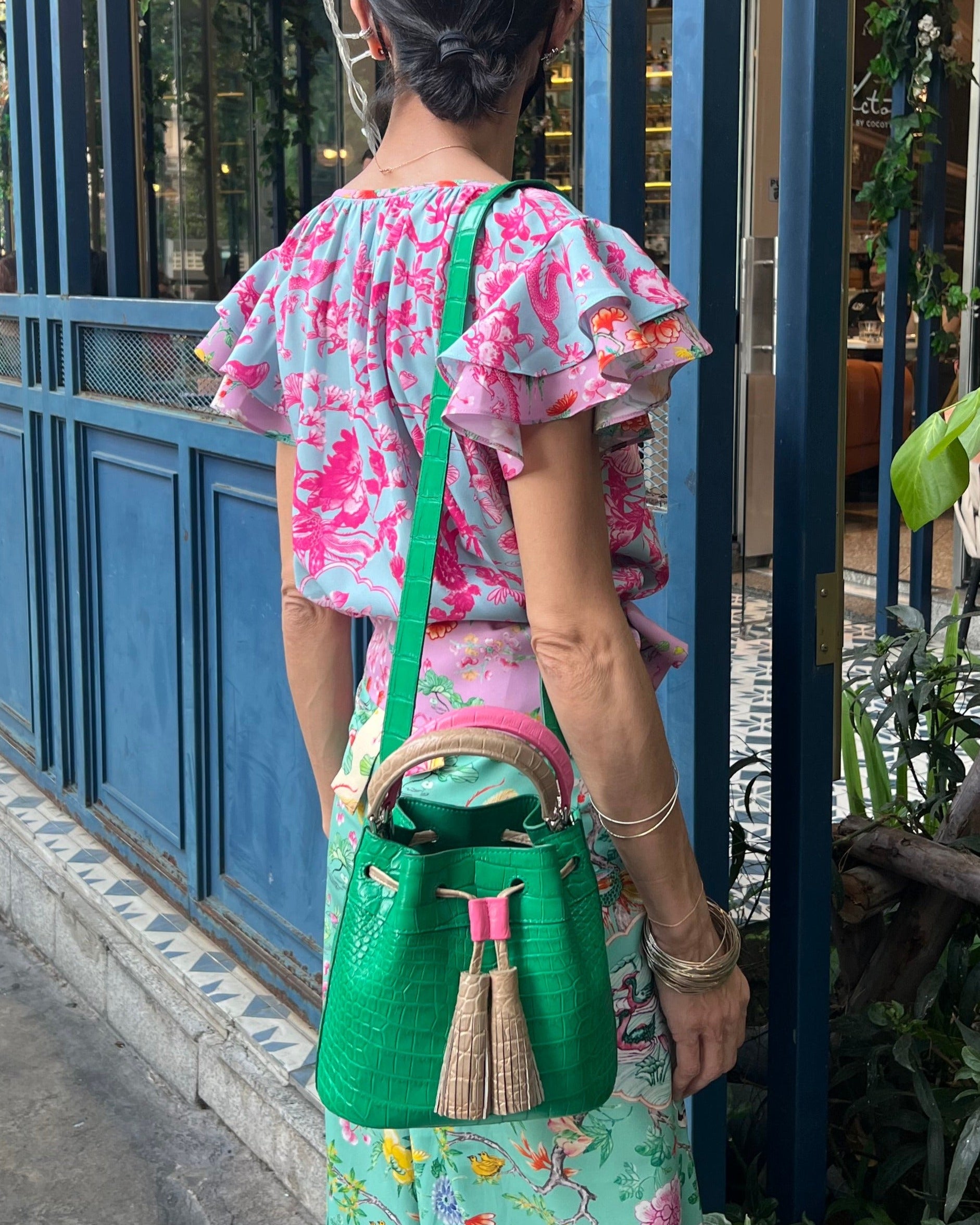 A woman wearing a floral green and pink dress with a seafoam green top handle bag with a wicker-like texture and a pink zipper.