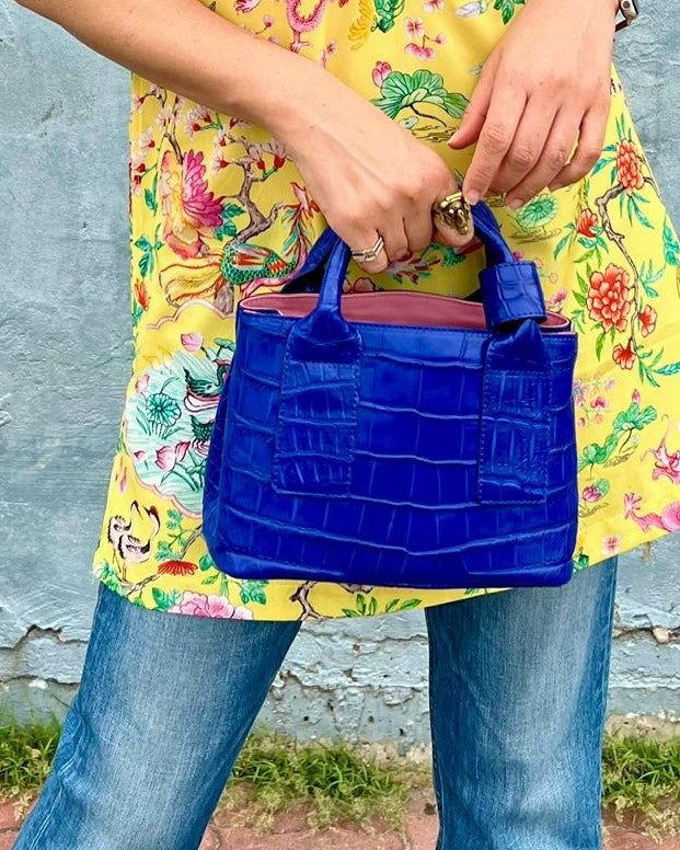 Person holding a blue handbag with a colorful floral-patterned garment in the background