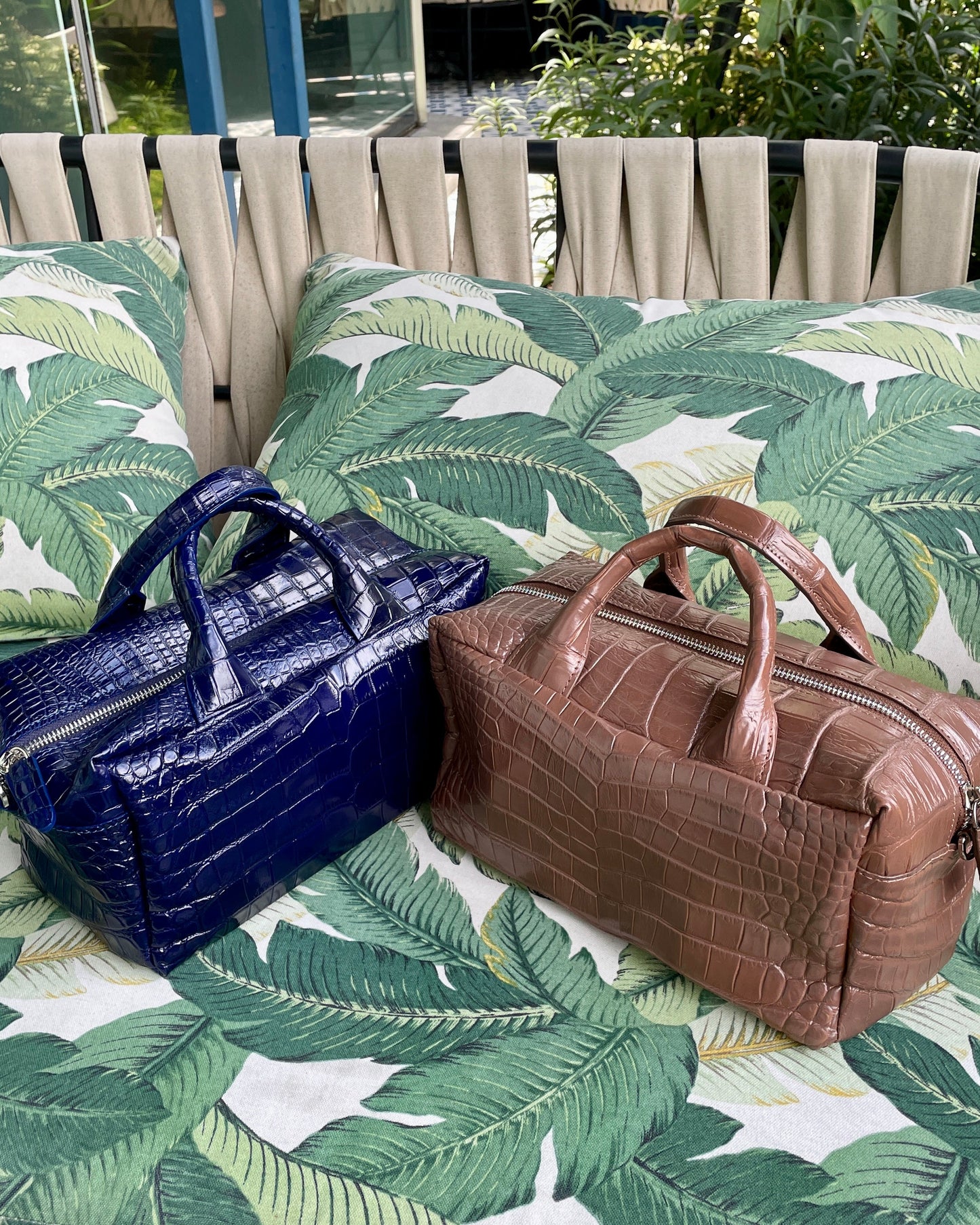 Two handbags, one blue and one brown, on a leaf-patterned surface.