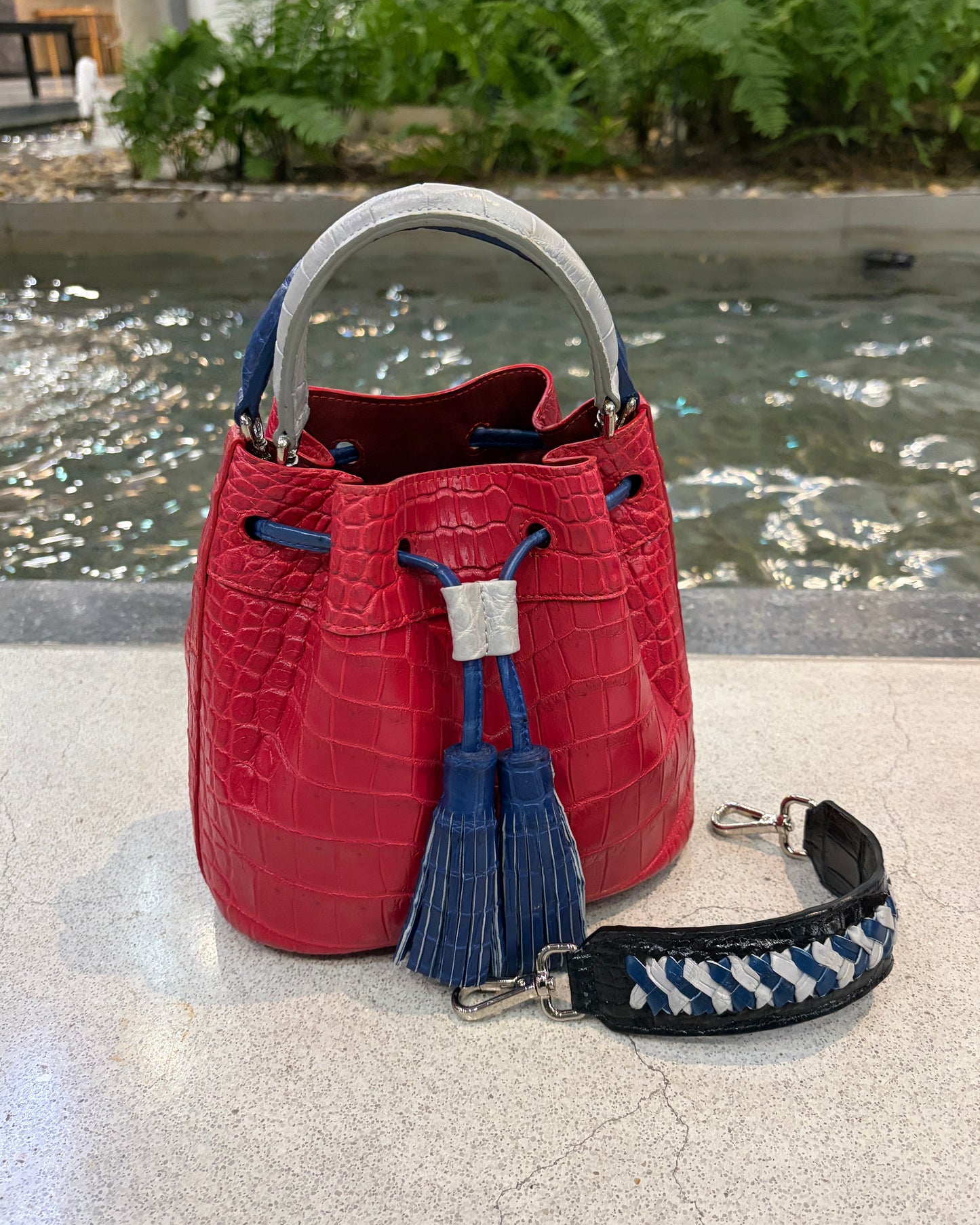 Red handbag with a blue tassel and strap on a concrete surface