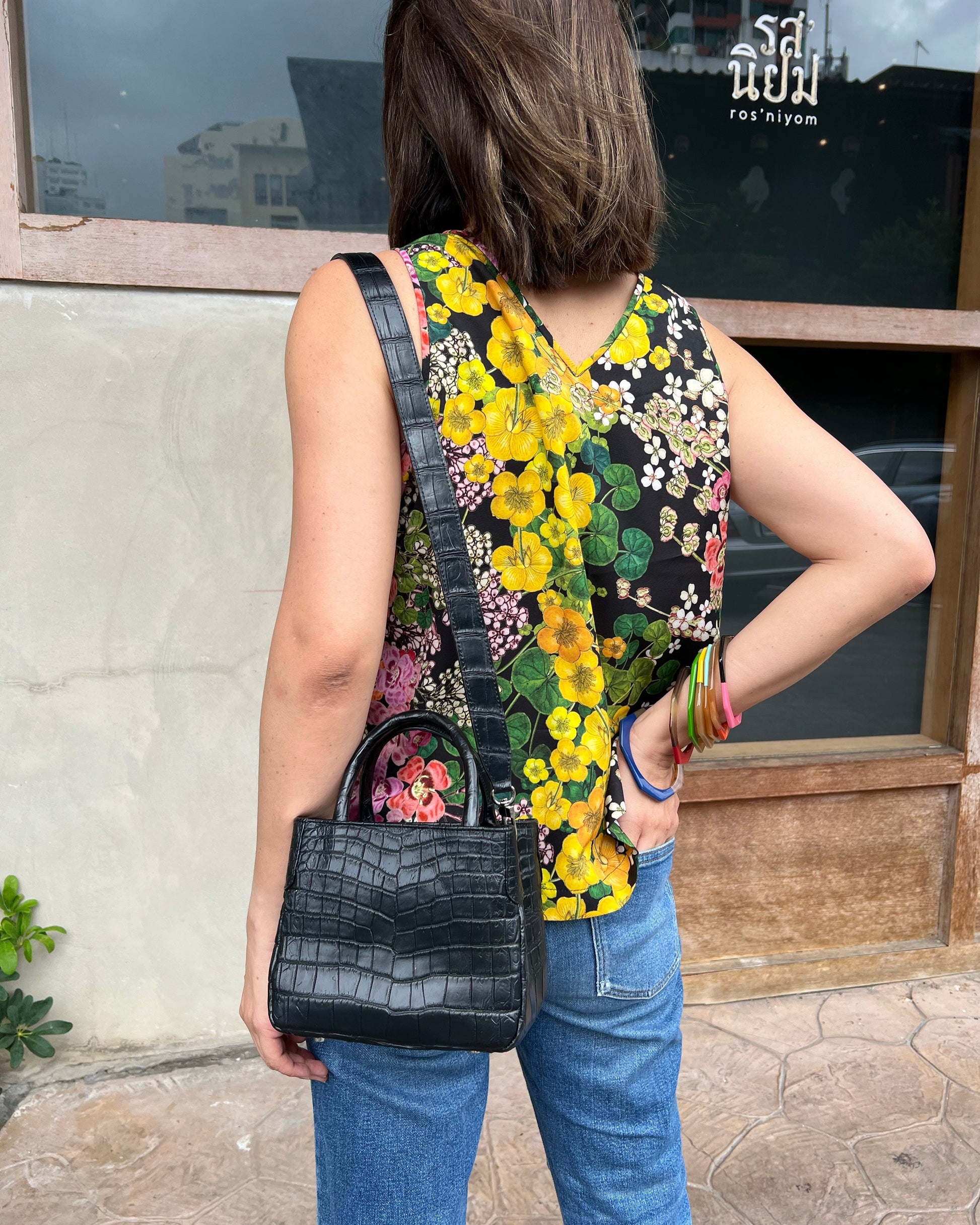 Person wearing a colorful floral dress holding a black handbag on a stone pavement.