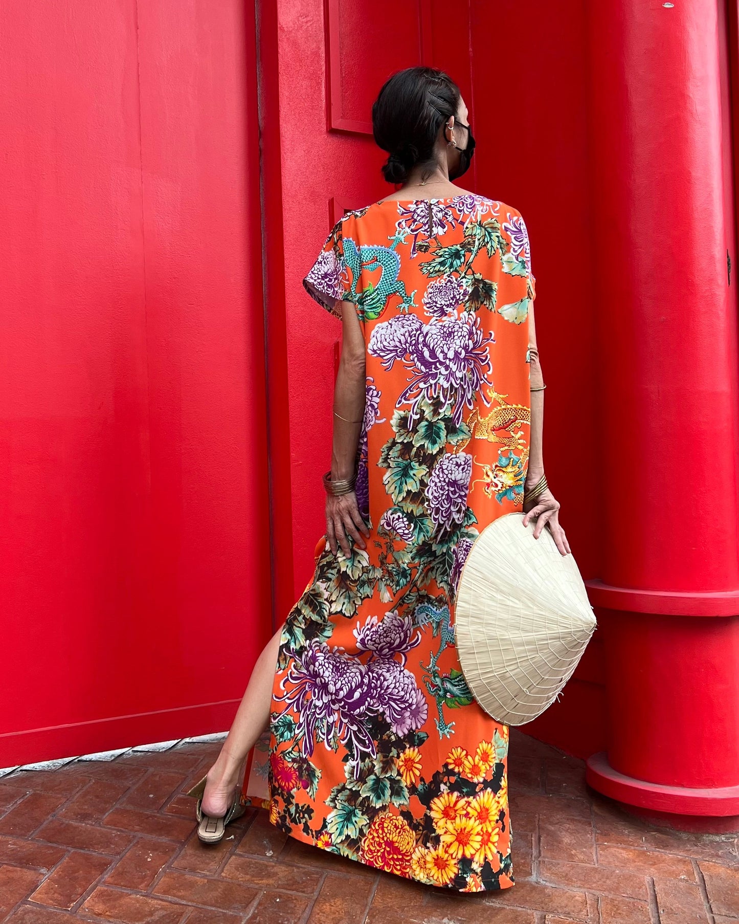 Woman in a colorful floral dress standing in front of a red door.
