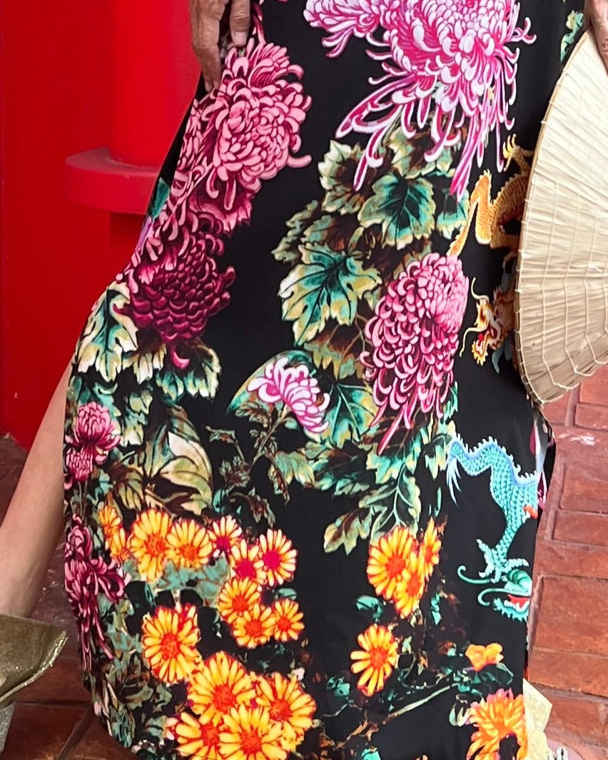 Person wearing a colorful floral dress with a dragon design against a red background