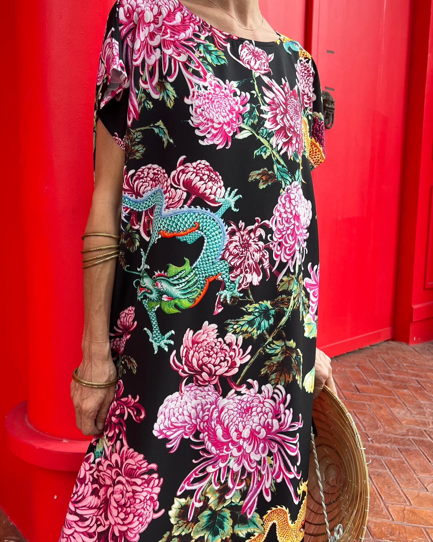 Person wearing a floral dress with dragon design against a red wall.