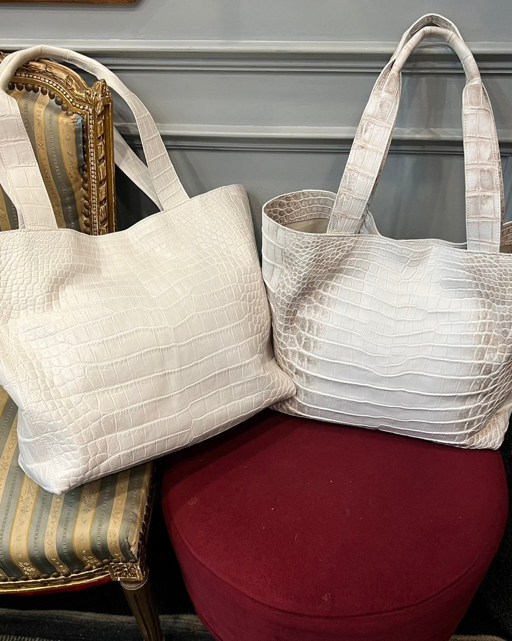 Two white textured handbags on a red cushion with a gray wall background