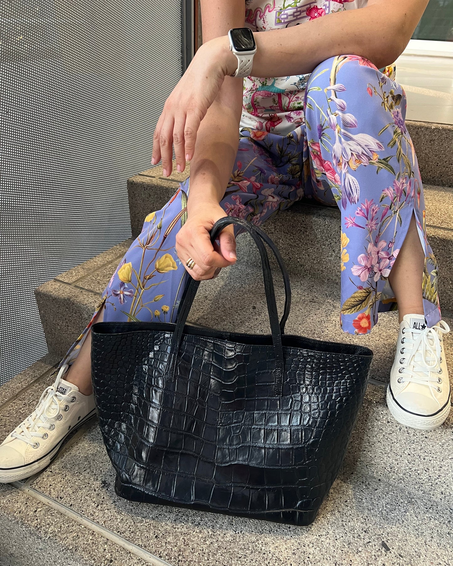 Person sitting on a step with a black crocodile-patterned handbag