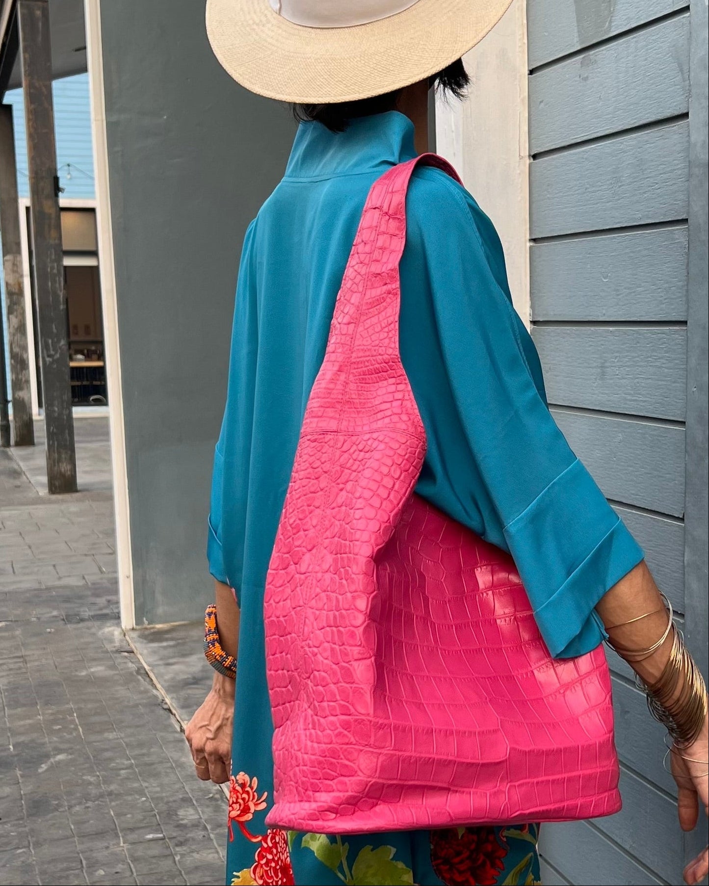 Person wearing a blue floral dress, pink shoulder bag leaning against a gray wall.