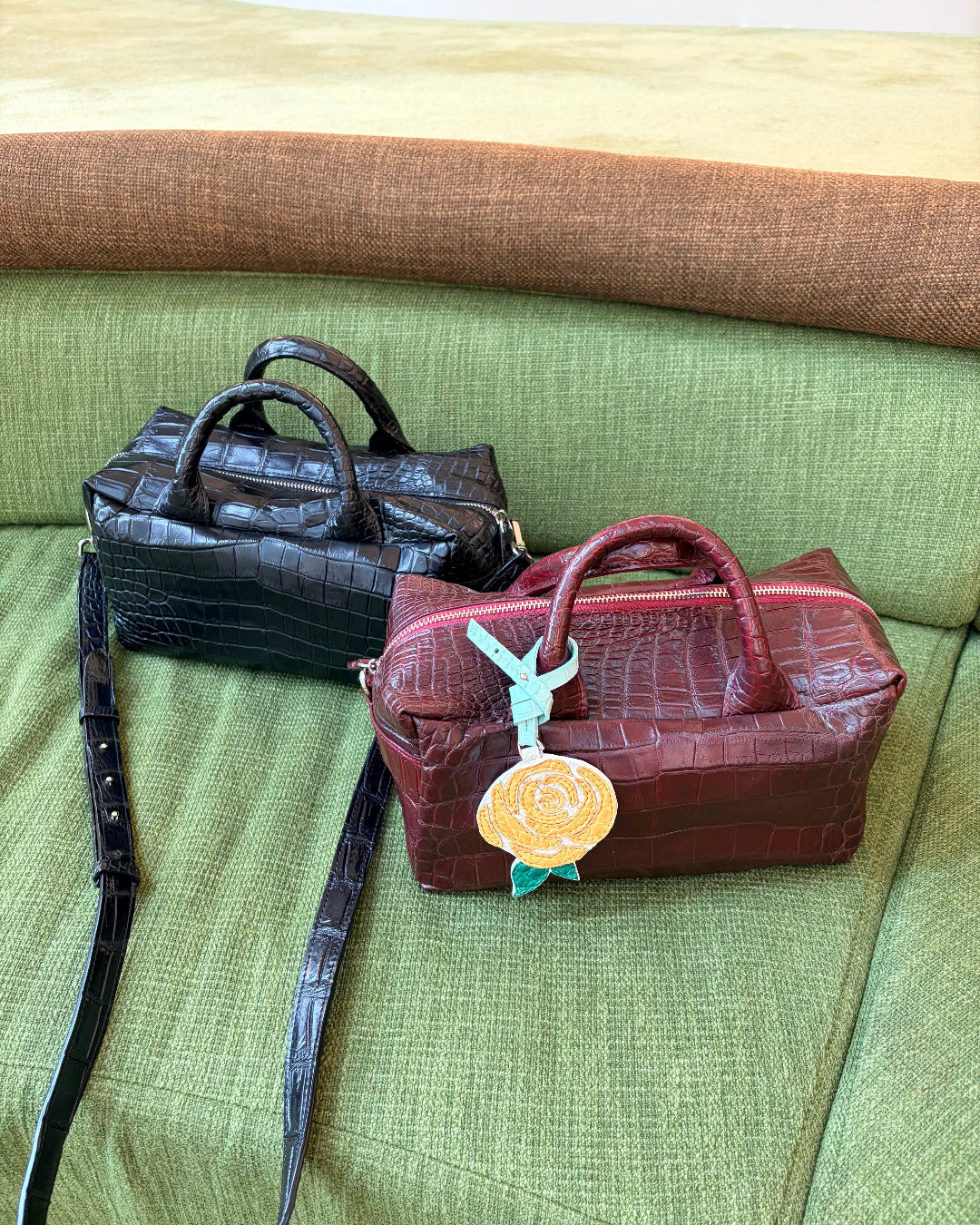 Two handbags, one black and one brown with a floral tag, on a green couch.