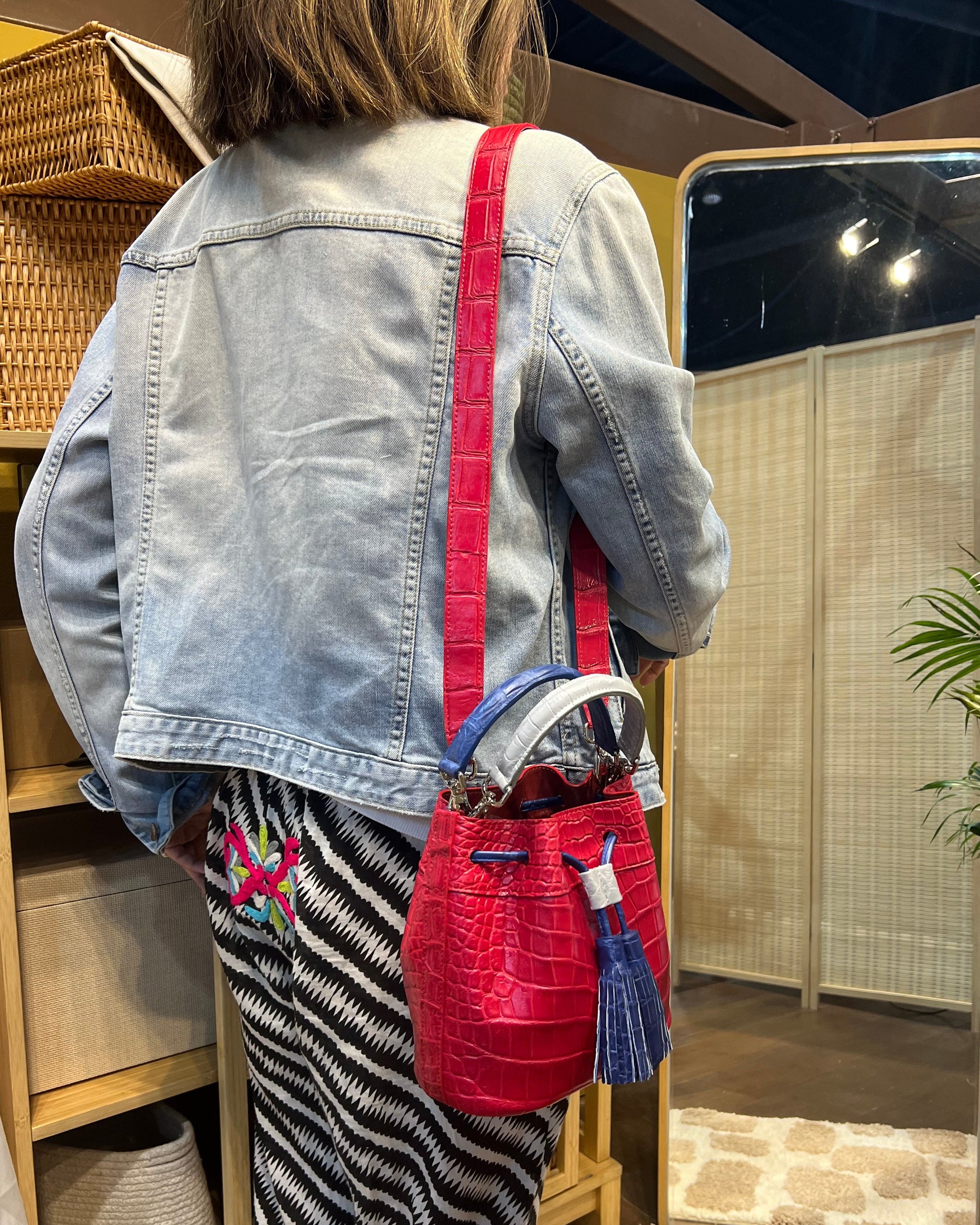 Person wearing a denim jacket with red accents and a striped skirt, standing in front of a mirror.