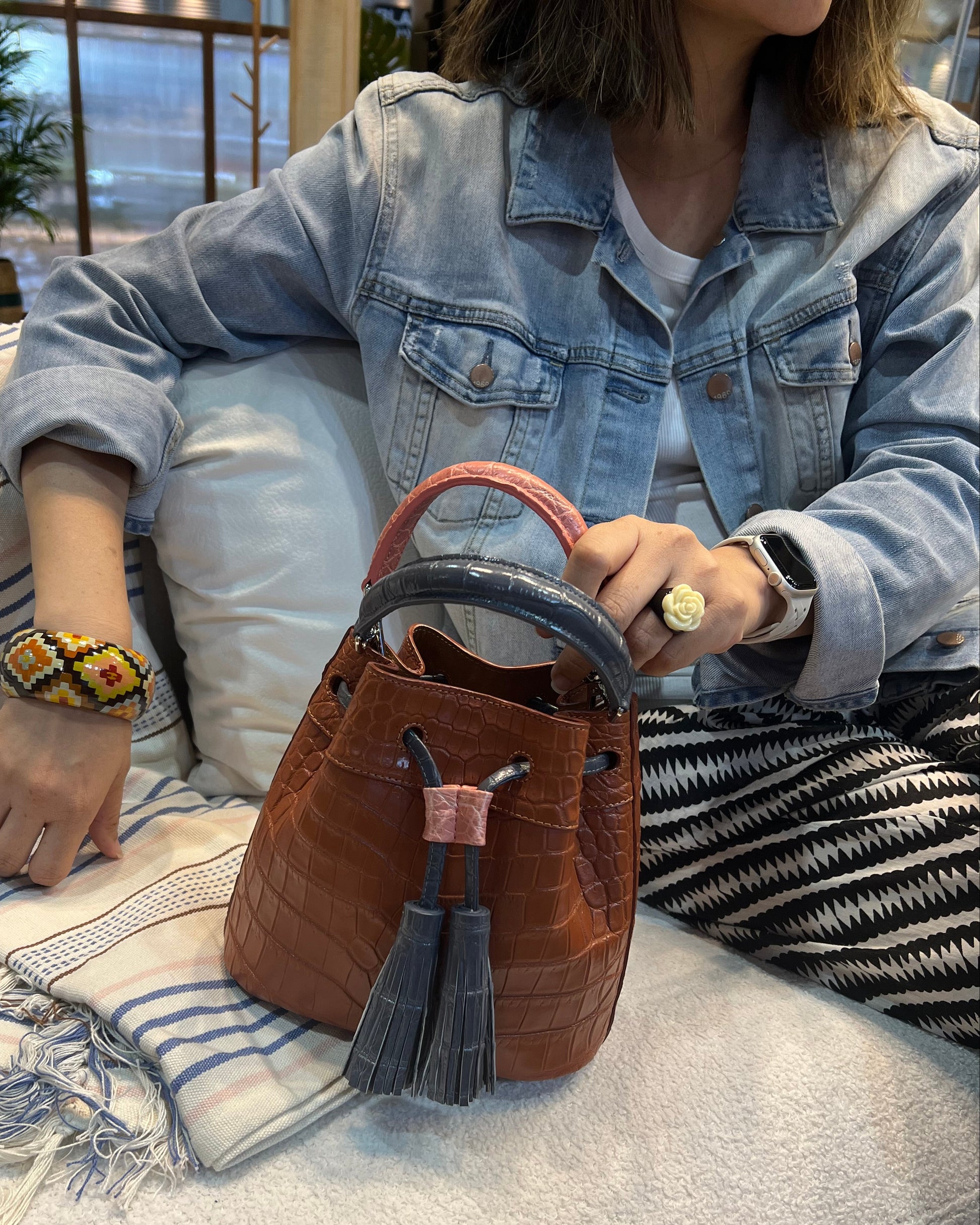 Person holding a brown leather bag with tassels on a light-colored blanket.