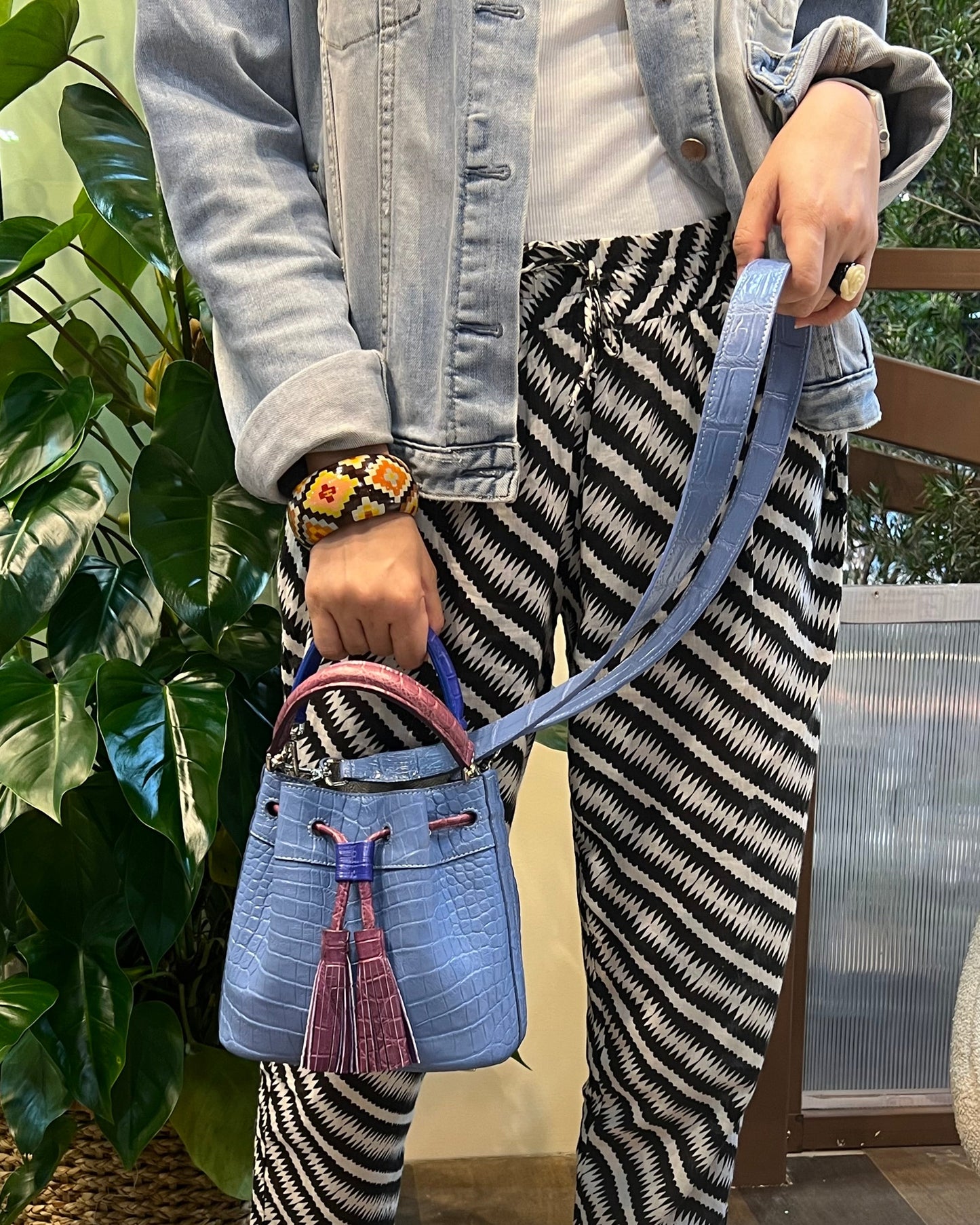 Person holding a blue handbag with striped pants and jeans in an outdoor setting