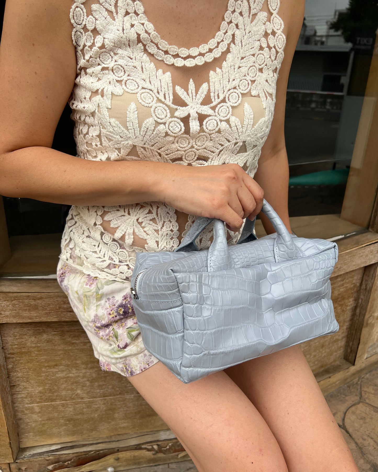 Person wearing a sheer lace dress with a textured gray bag on a wooden surface.