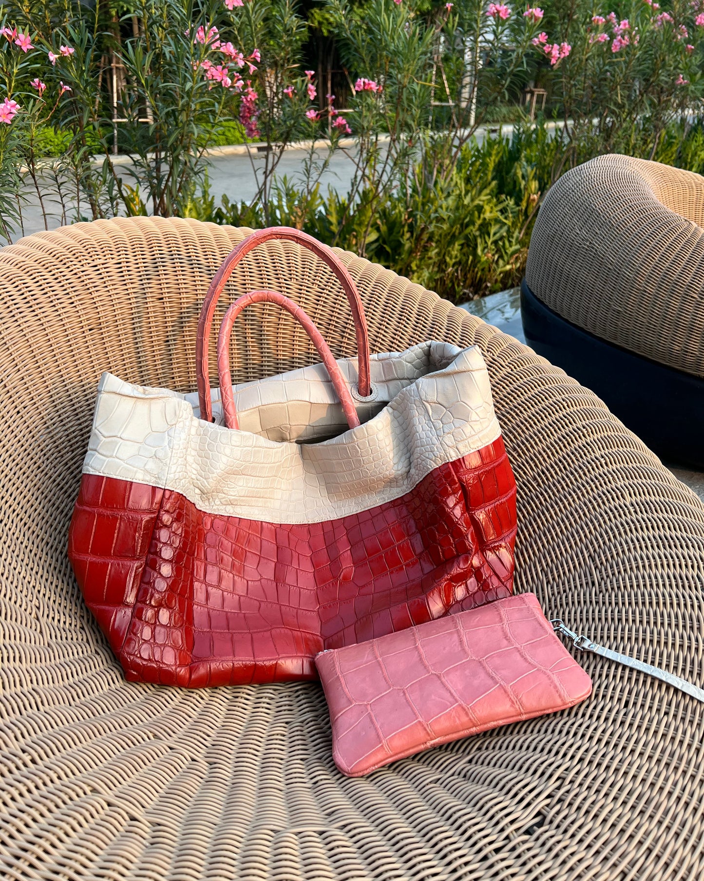 Color-blocked handbag with red, white, and pink sections on a wicker chair outdoors.