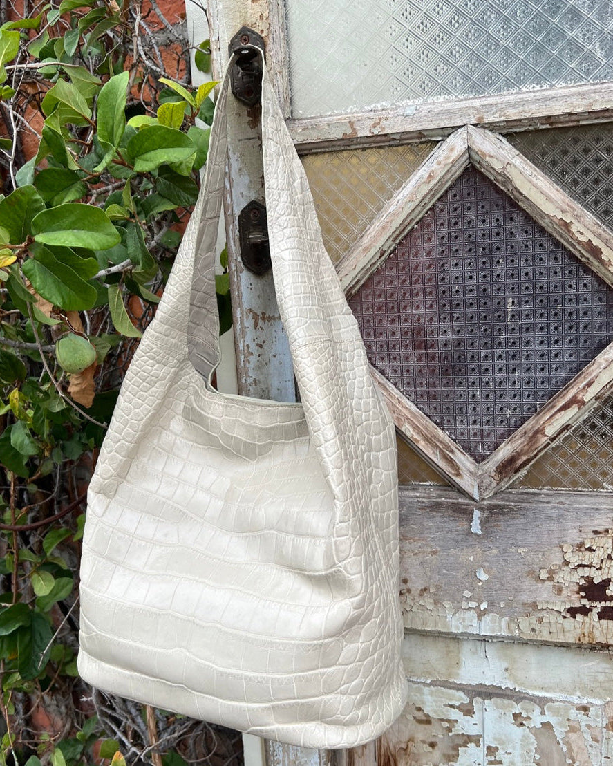White textured handbag hanging on a rustic wooden door with greenery in the background