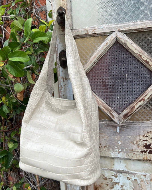 White textured handbag hanging on a rustic wooden door with greenery in the background
