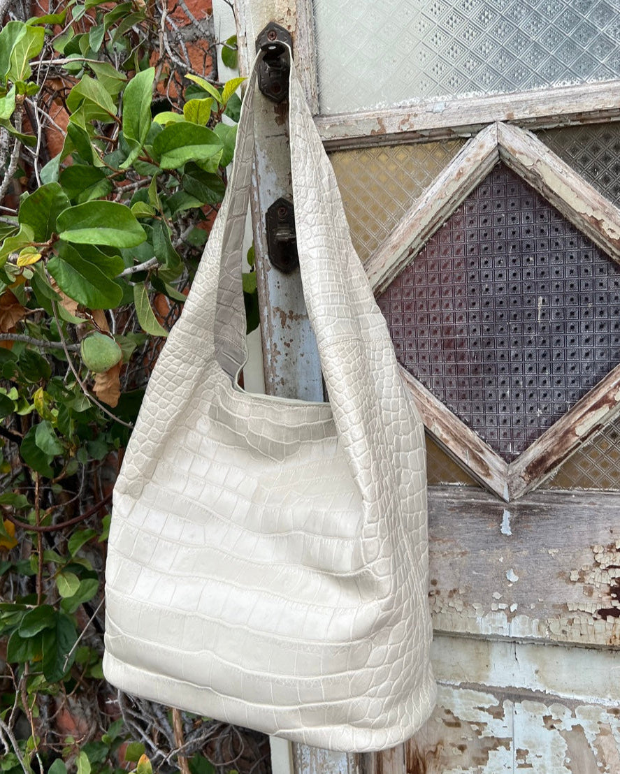 White textured handbag hanging on a rustic wooden door with greenery in the background