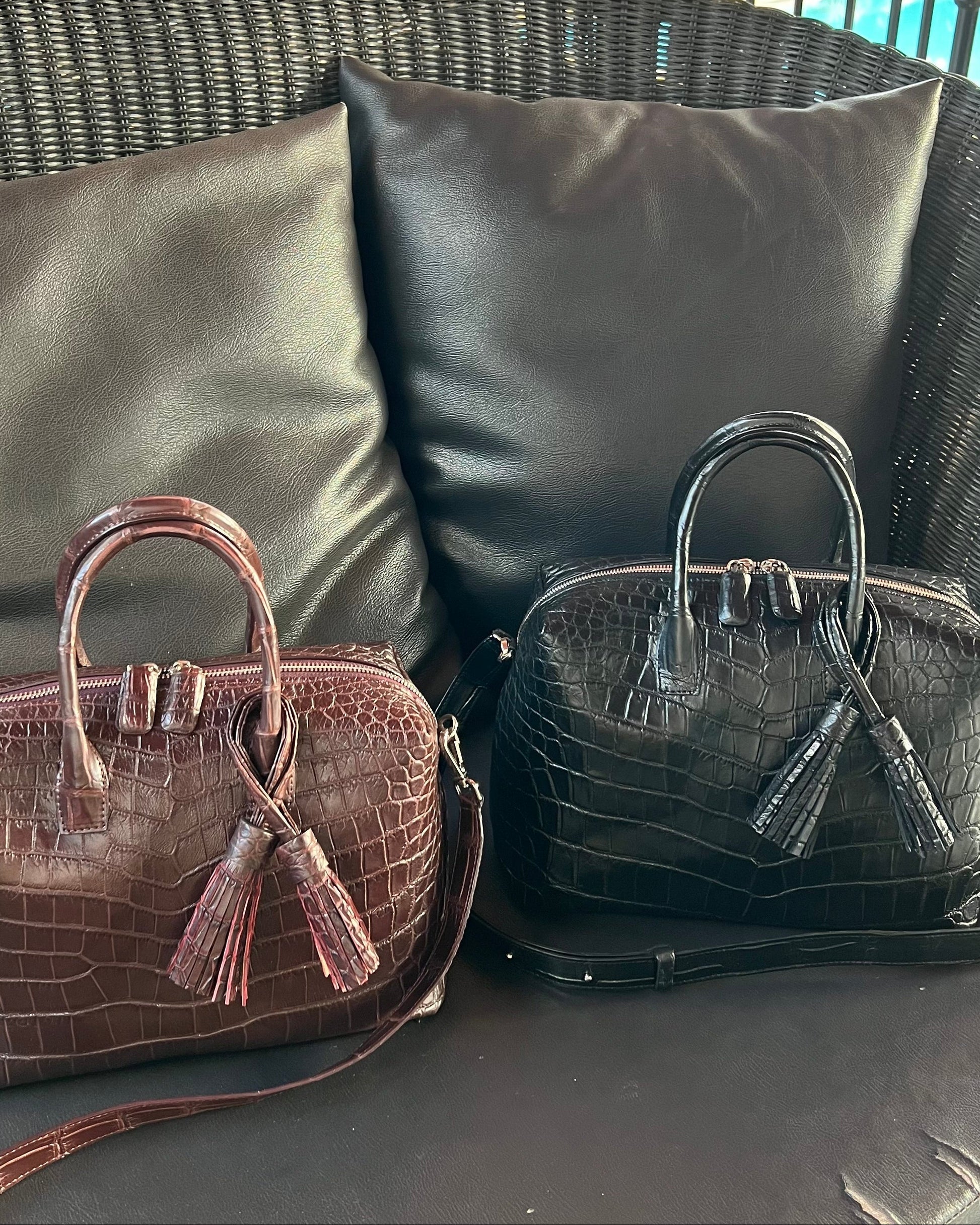 Two handbags, one brown and one black, on a wicker chair with a pool in the background.