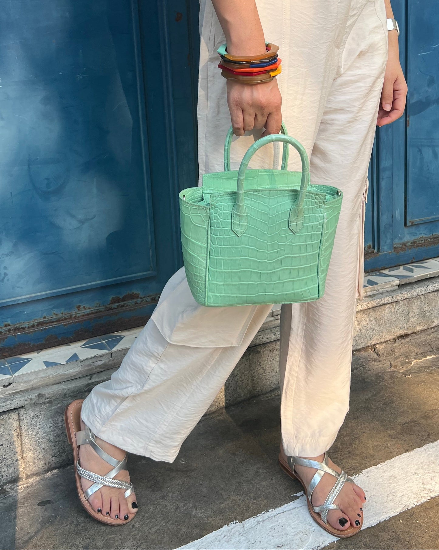 Person holding a green handbag on a street with a blue door in the background