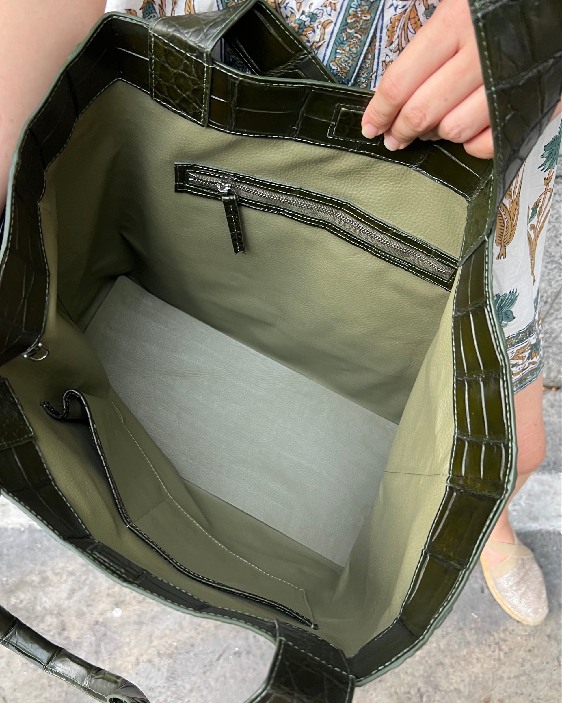 Green leather bag with a zipper held by a person on a textured surface