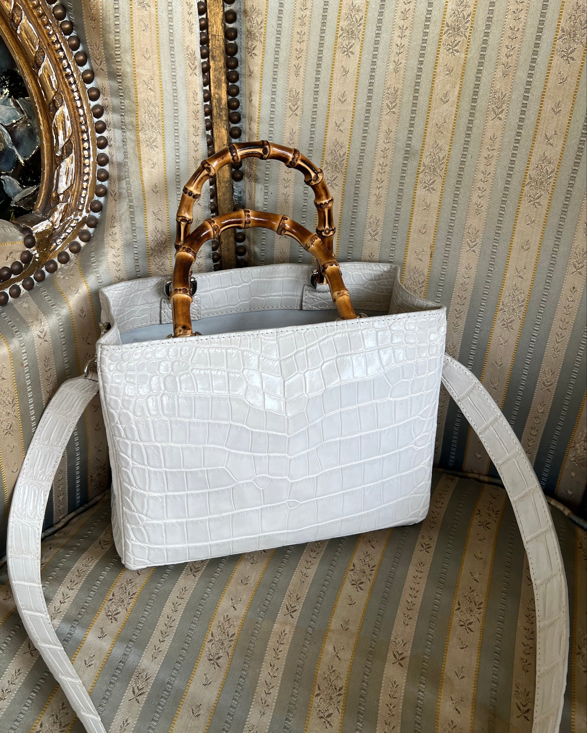 White textured handbag with gold handle on a decorative wall background