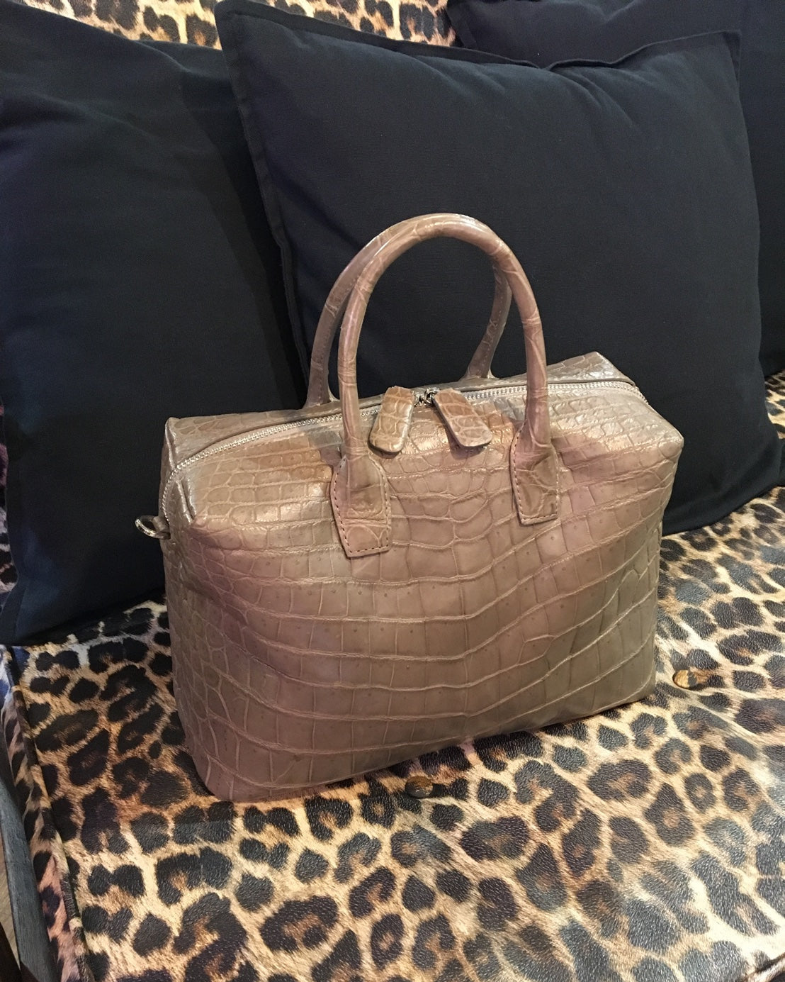 Brown textured handbag on a leopard print surface with black cushions in the background