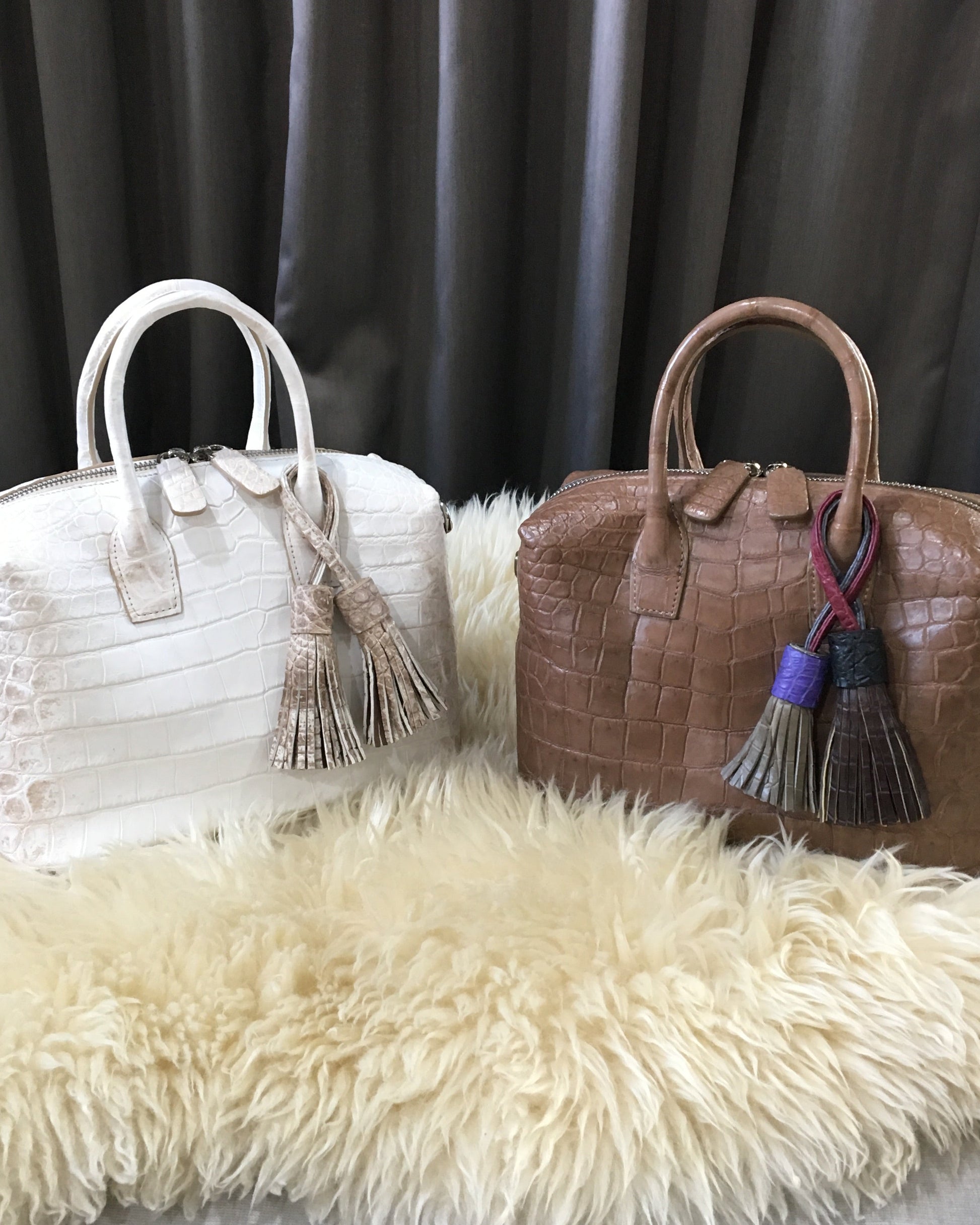 Brown textured handbag with tassel and white textured handbag with tassel on a fluffy white surface.