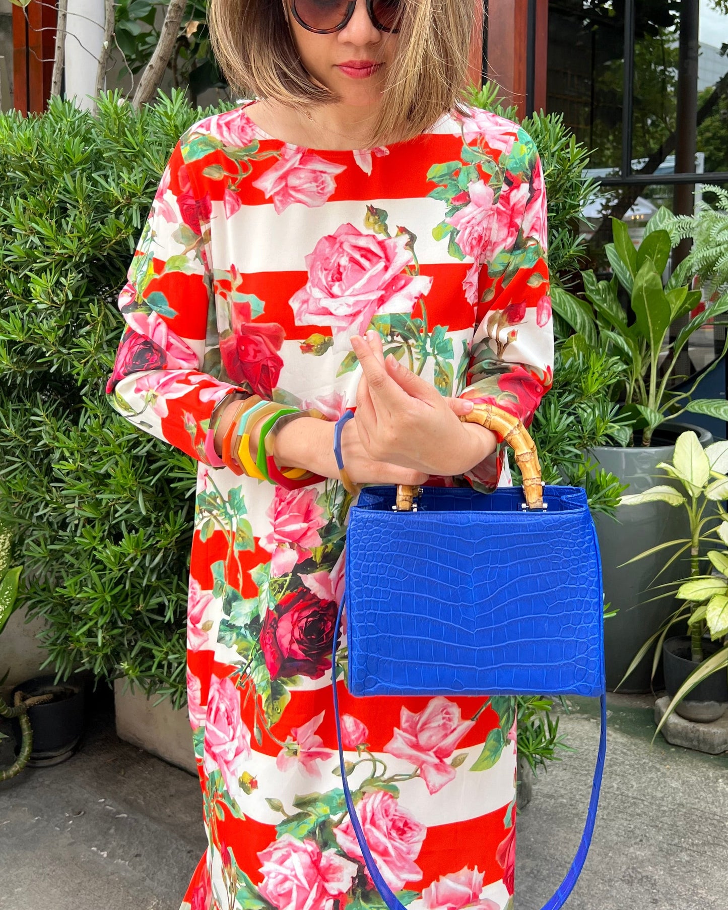 Person wearing a colorful floral dress holding a blue handbag outdoors.