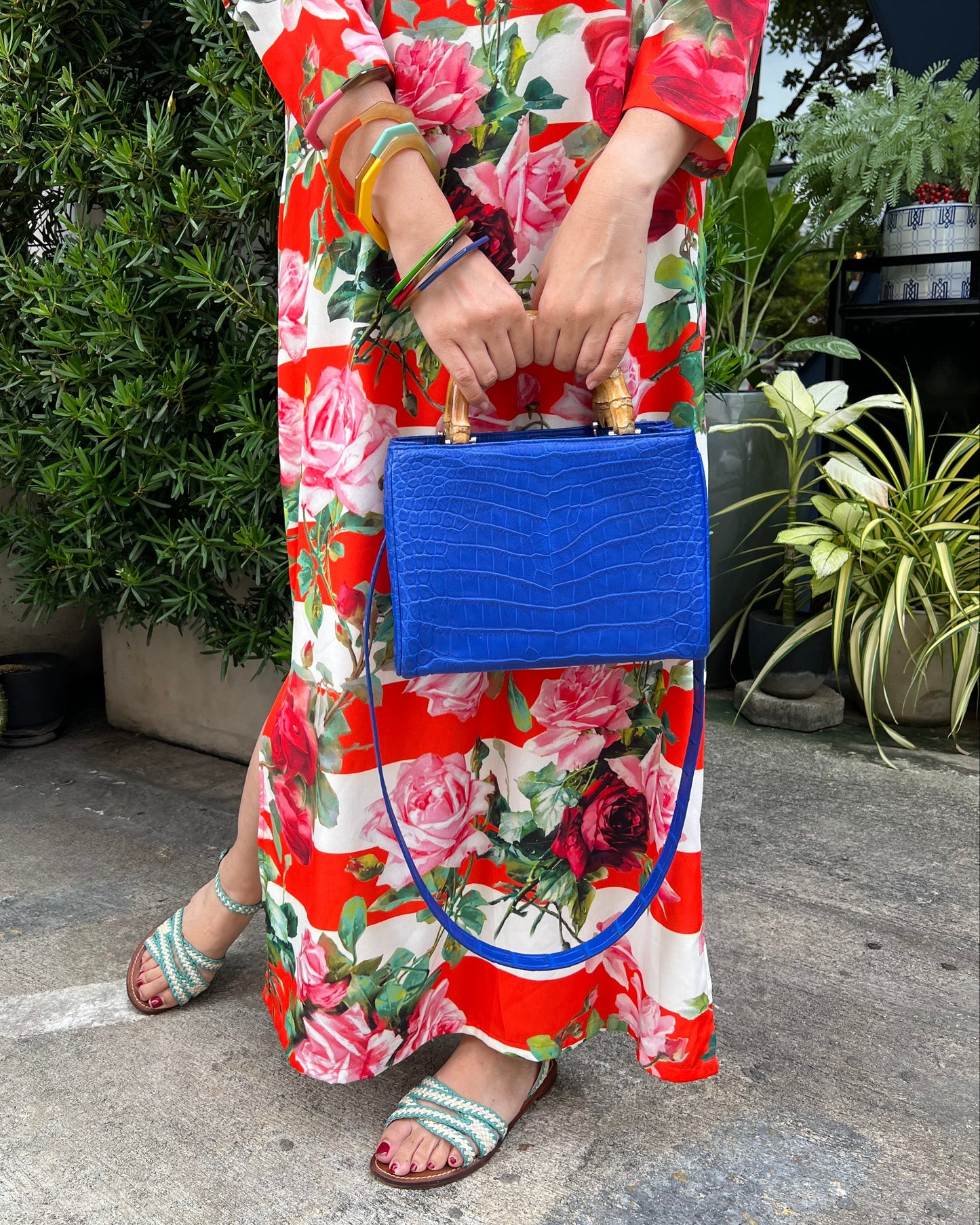 Person wearing a colorful floral dress holding a blue woven bag on a street.