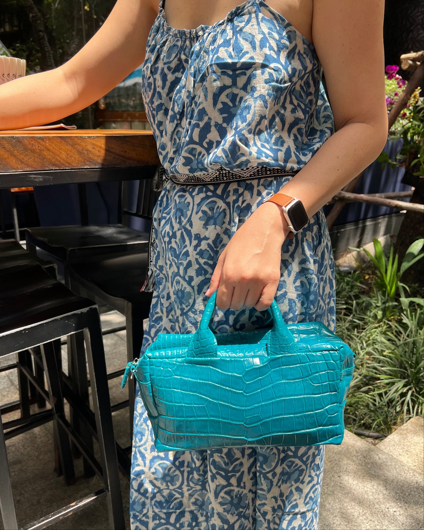 Person holding a blue handbag with a patterned dress and watch.