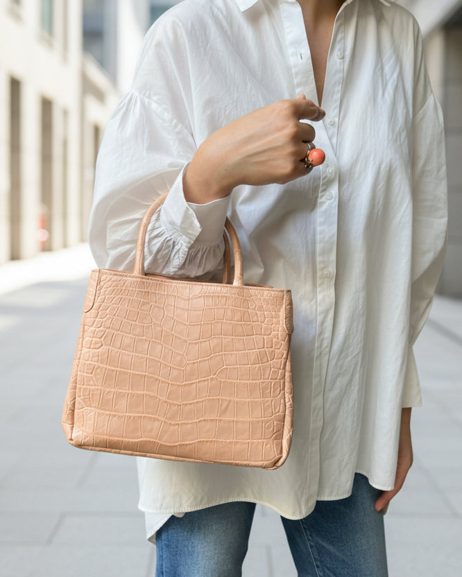 Person holding a beige crocodile-patterned handbag in an outdoor setting
