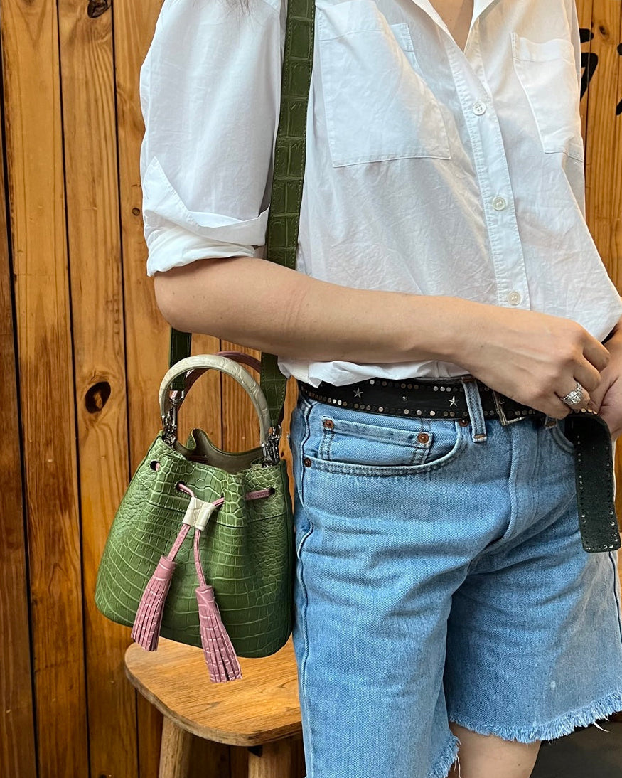 Person wearing a white shirt and blue shorts holding a green handbag against a wooden background