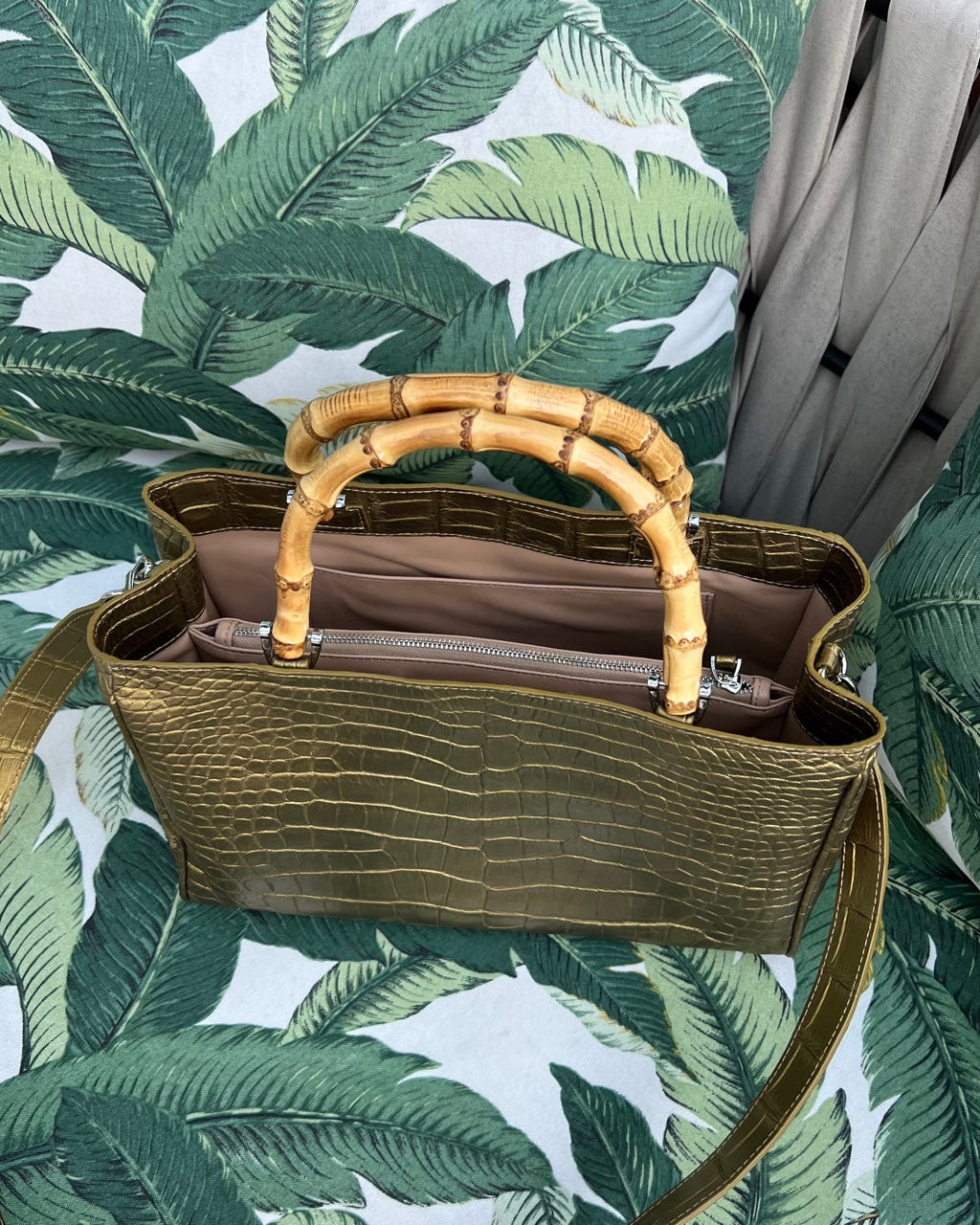 Gold handbag with bamboo handles on a leaf-patterned background