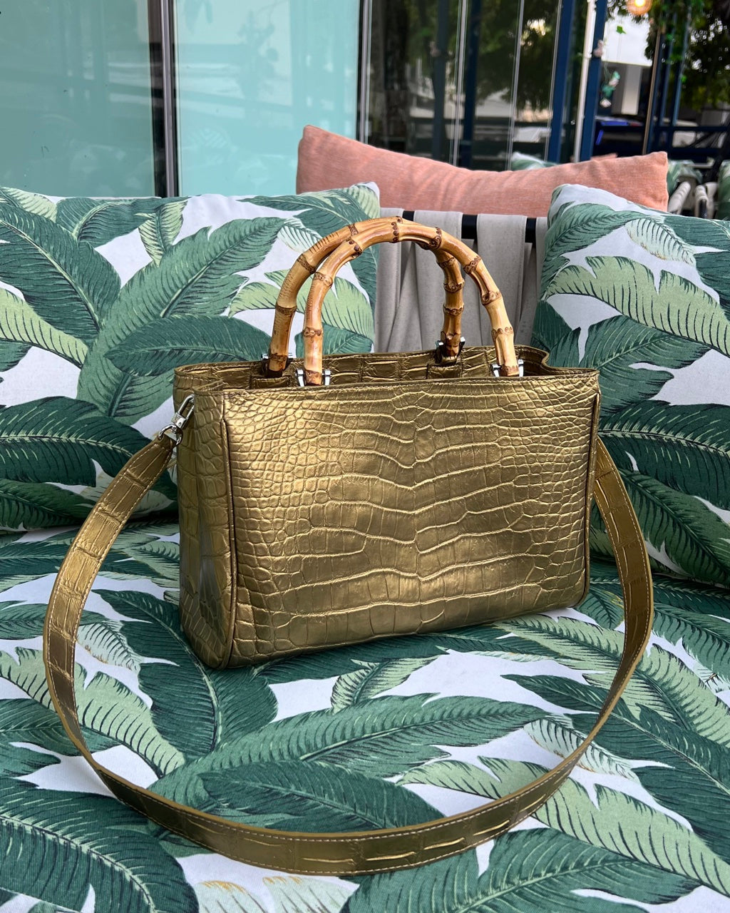 Gold handbag with bamboo handle on a green leaf-patterned surface