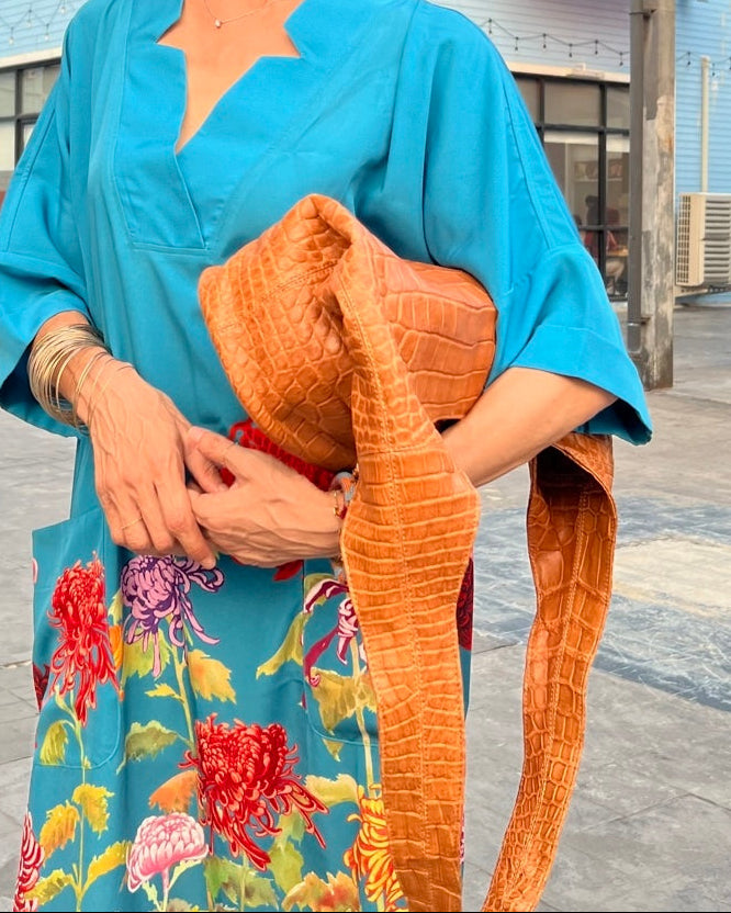 Person wearing a blue floral dress holding an orange textured bag outdoors.