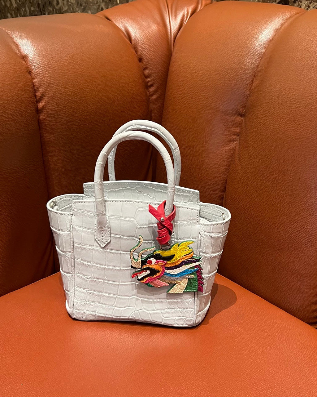 White handbag with colorful dragon design on a brown leather couch